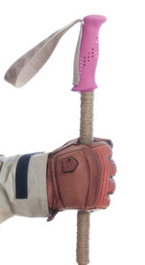 Hand with brown leather glove holding a bamboo ski pole with pink grip and grips extension of hemp cord.