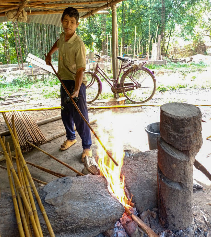 An artisan is roasting Calcutta canes over open fire to get dark tanned bamboo.
