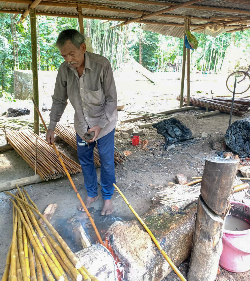 En hantverkare värmer upp Calcuttabambu över glöd så att den kan rätas med hjälp av stubben bredvid.
