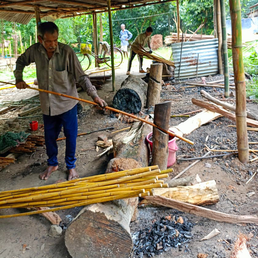 An artisans is straightening a Calcutta bamboo cane using a jack in a trunk.