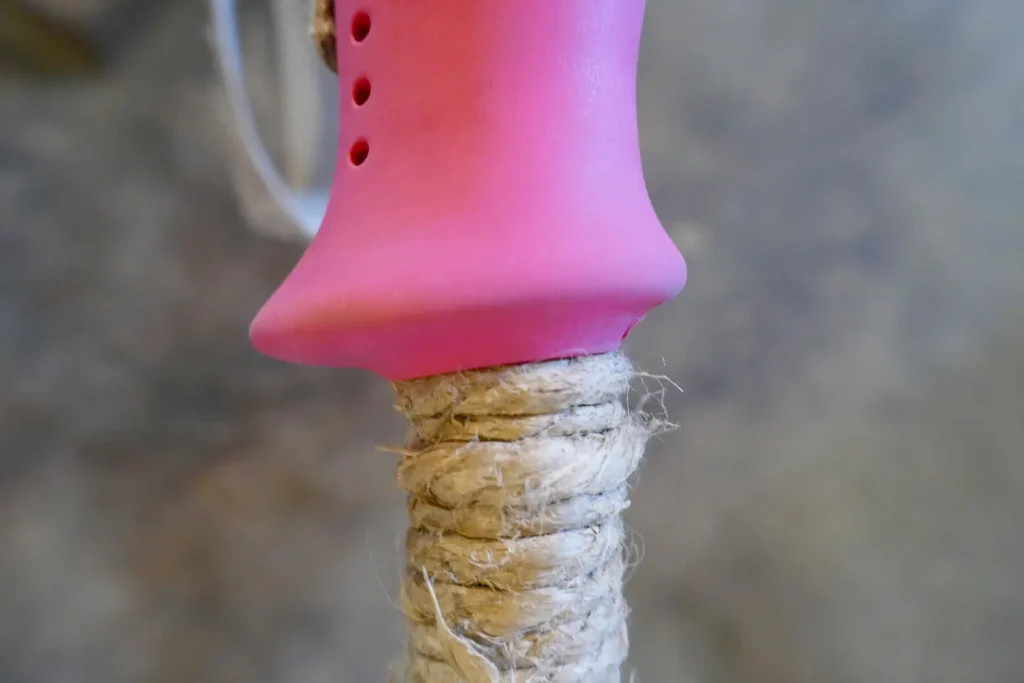 Close-up of a ski pole with a pink handle and an extended grip made of wrapped hemp twine.