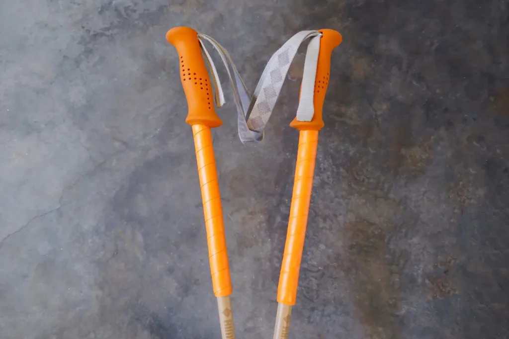 A pair of ski poles with orange grips and extensions of orange overgrip tape.