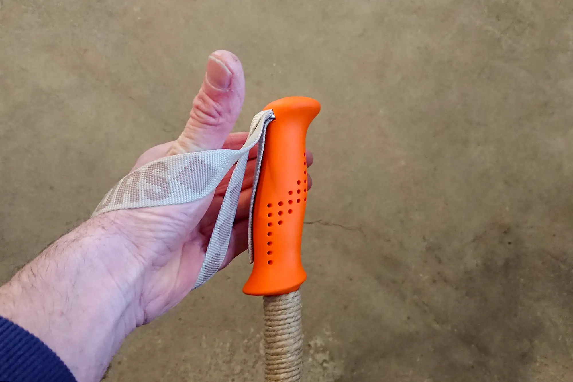 Hand som är på väg att greppa en skidstav med orange handtag.