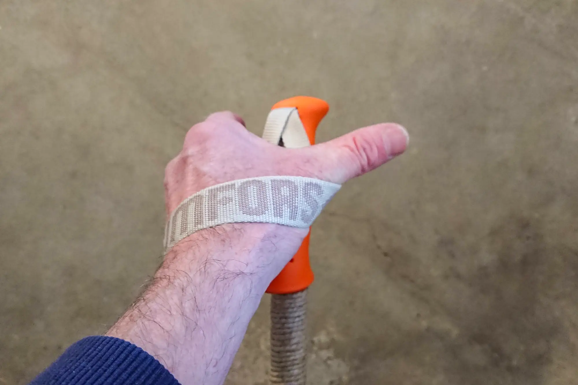 Hand som är på väg att greppa en skidstav med orange handtag.