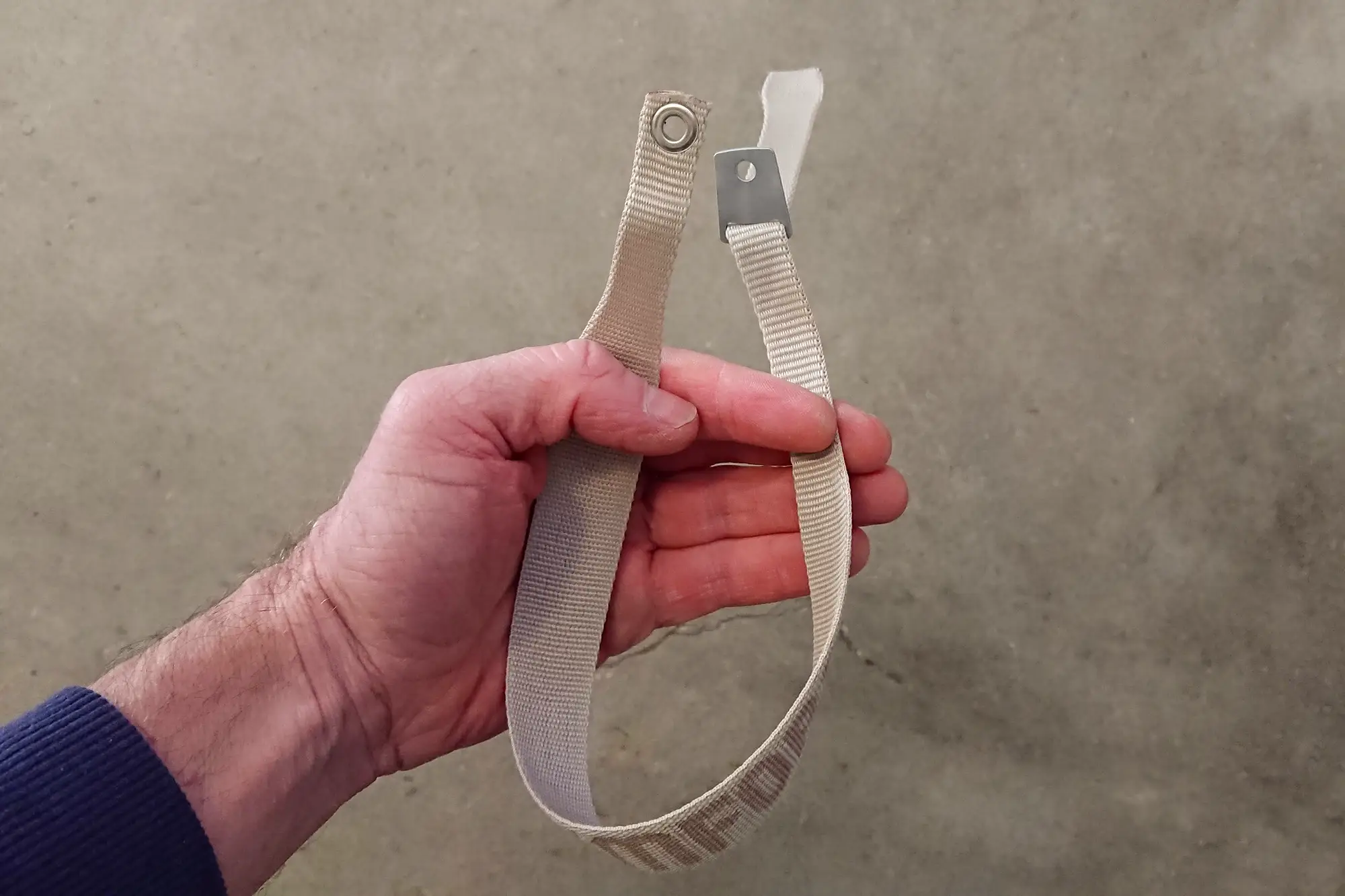 En hand håller upp en beige handrem till en skidstav.