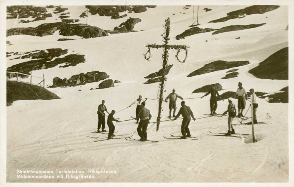 Skidåkare “dansar” runt midsommarstången I Riksgränsen 1938. En dam bär bikini.