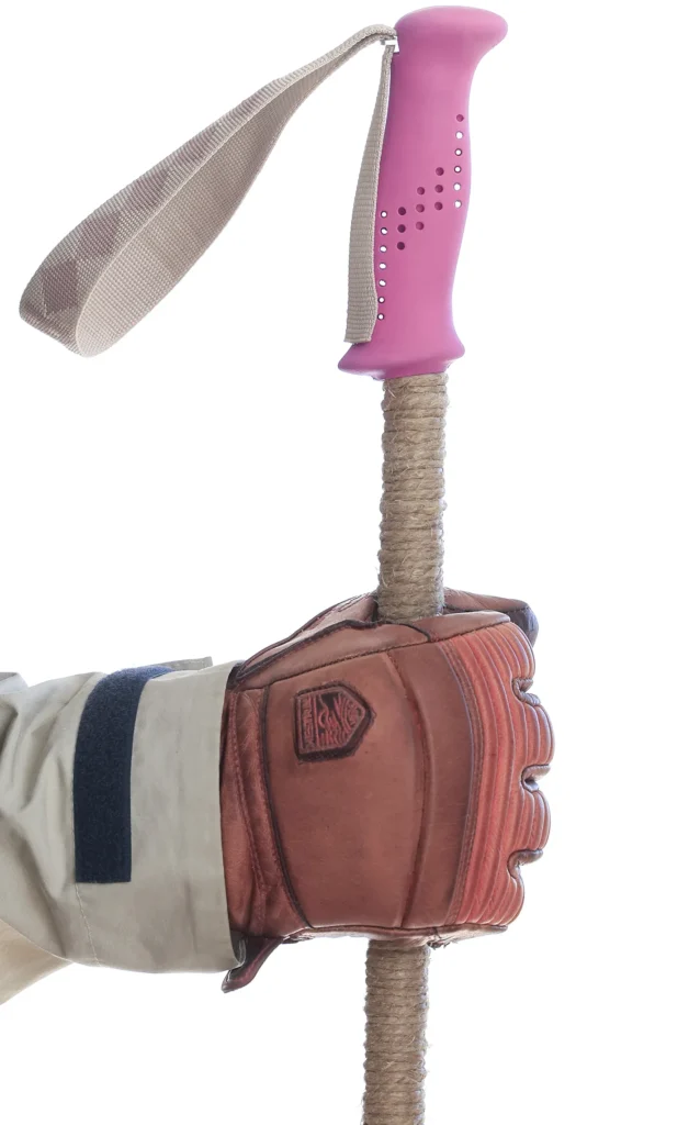 Hand with brown leather glove holds a ski pole with pink grip and extended grip f wound hemp twine.