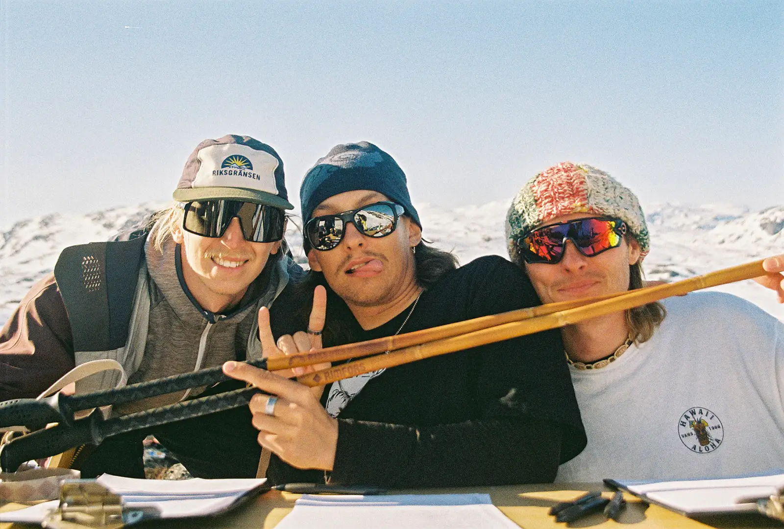 Three guys in sunglasses holding a pair of bamboo ski poles.