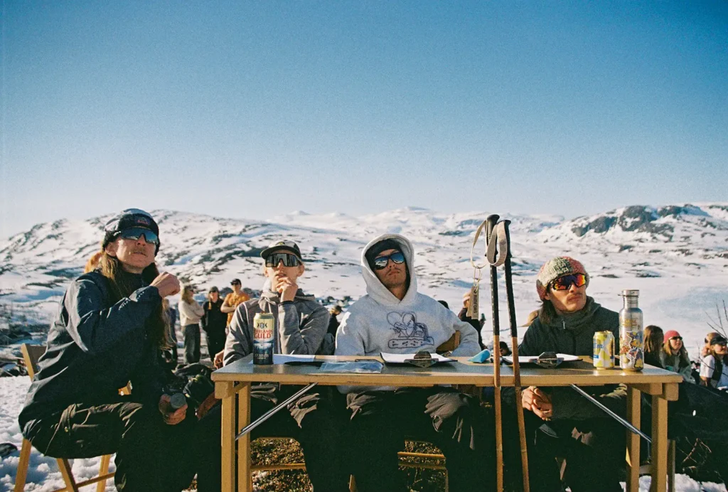Four guys in sunglasses sit at a jury table watching a freeride competition.
