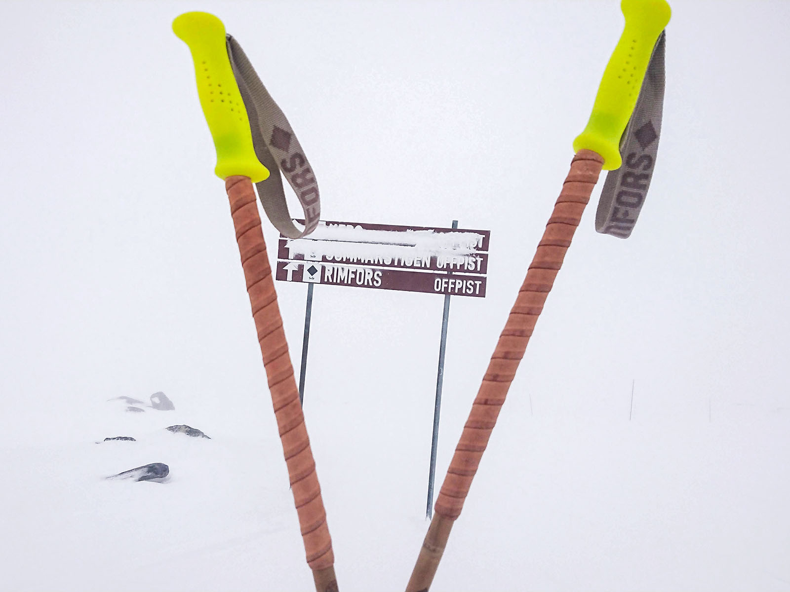 Fluorescent yellow bamboo ski poles with grip extensions of bark tanned reindeer leather, in front of the Rimfors black diamond off-piste run in Riksgränsen.