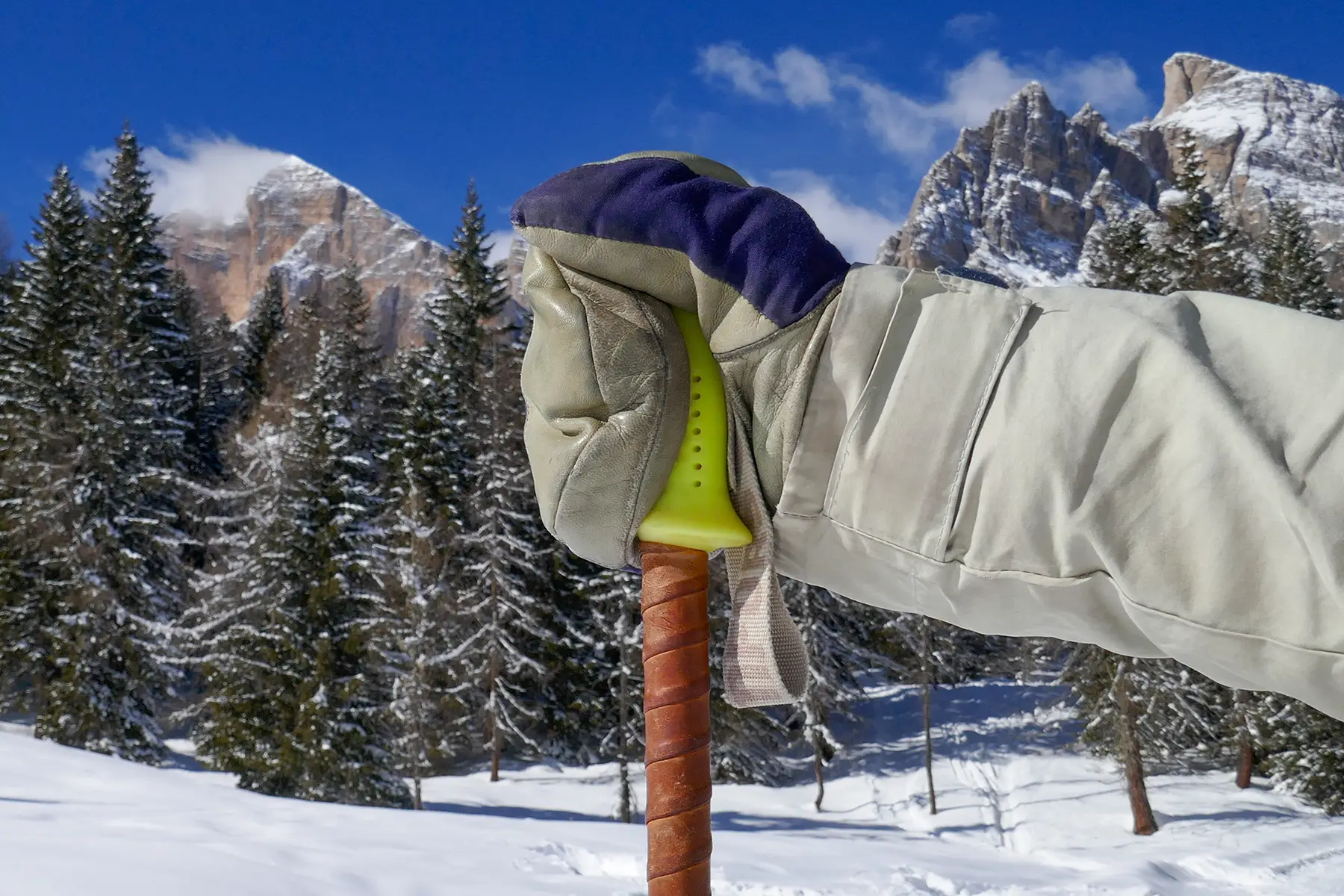En hand håller en skidstav utan att ha handremmen runt handloven. Dolomiterna Tofana-berg i bakgrunden.