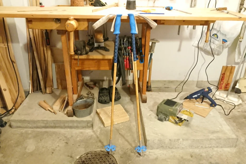 Bamboo ski poles with blue grips and baskets leaning towards a work bench.