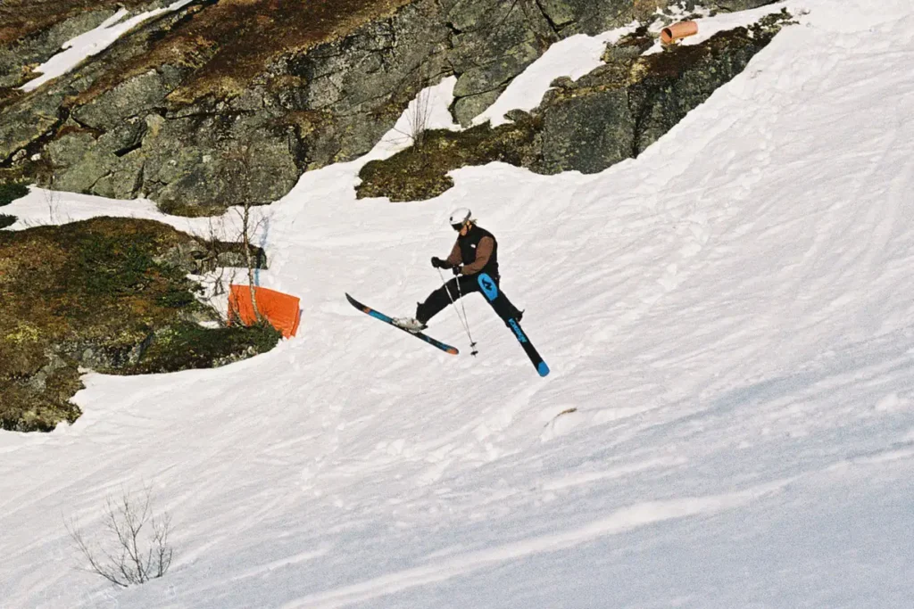 A skier in a white helmet does a classic spread eagle with the poles between the legs.