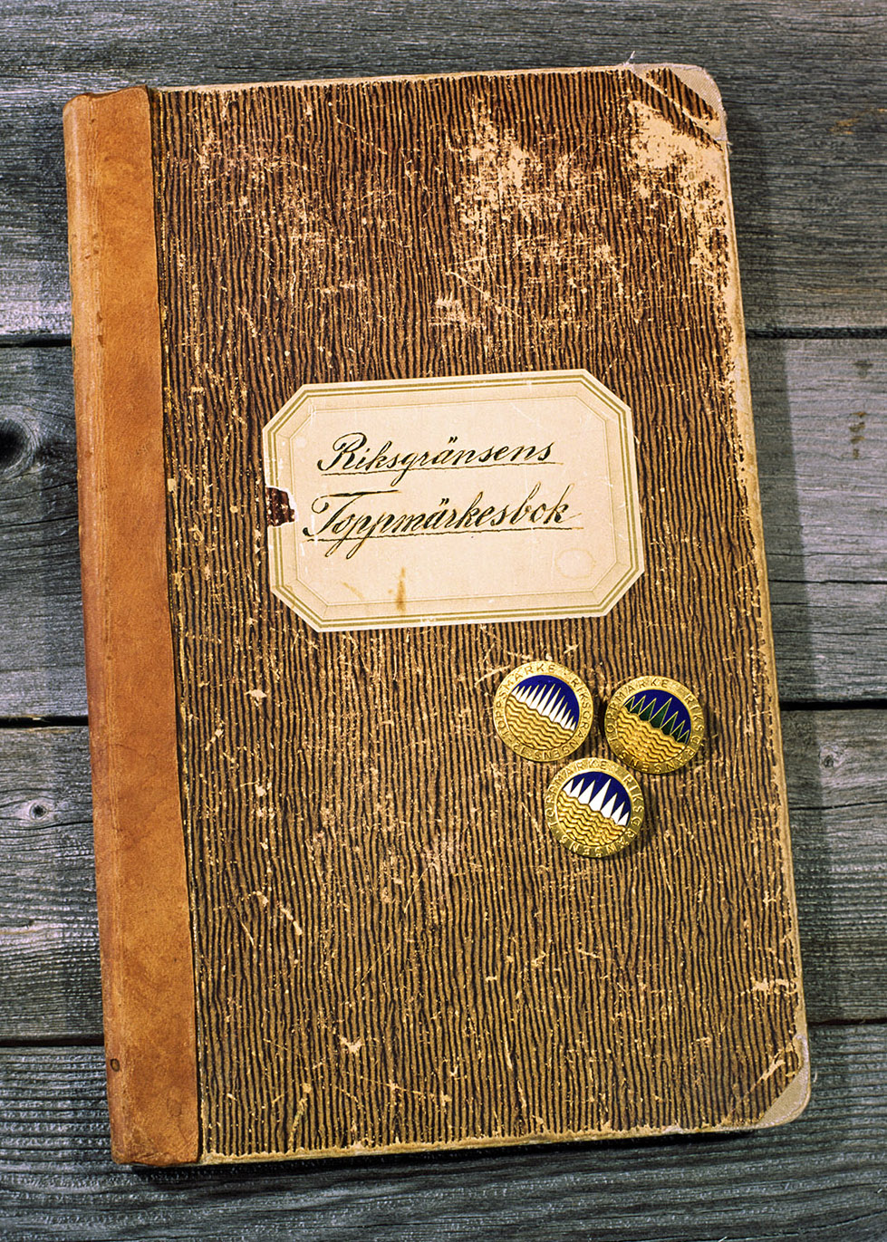 Riksgränsen’s Summit badge book with the badges for twelve and seven white peaks respectively, as well as the summer version with seven green peaks.