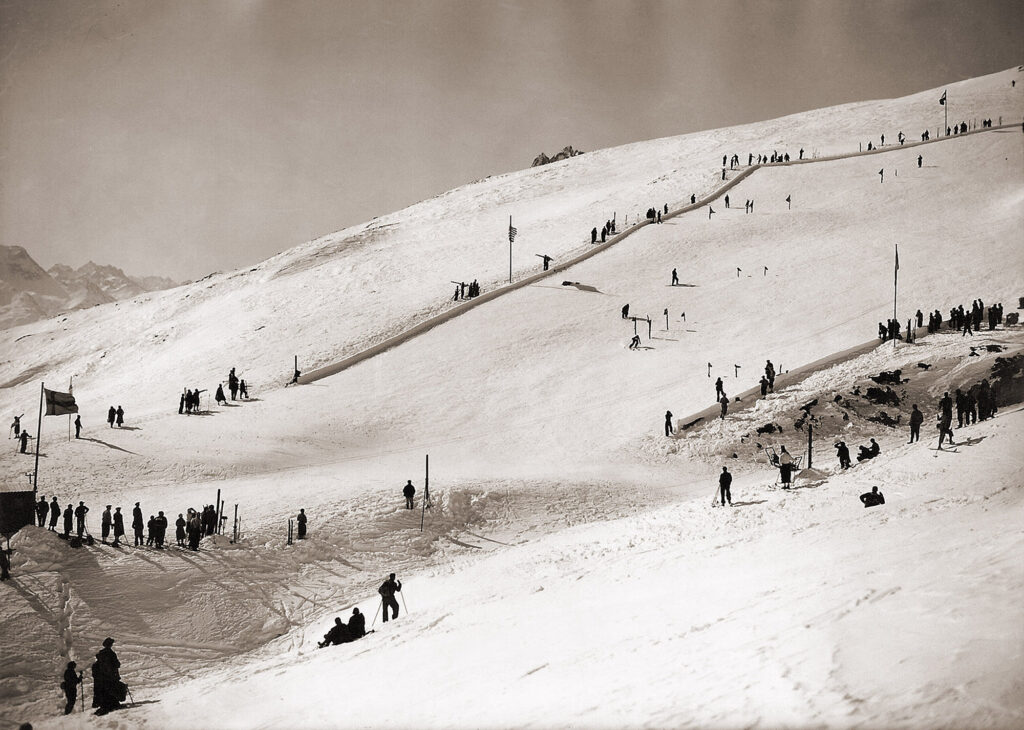 Även på damernas slalom under VM 1934 användes de vikbara Kandaharflaggorna. Här syns också några av de stora grövre portarna som skidpionjären Hannes Schneider fått in i tävlingsbanan för att utesluta tvivelaktigheter om en tävlande verkligen passerat porten eller bara åkt över den.